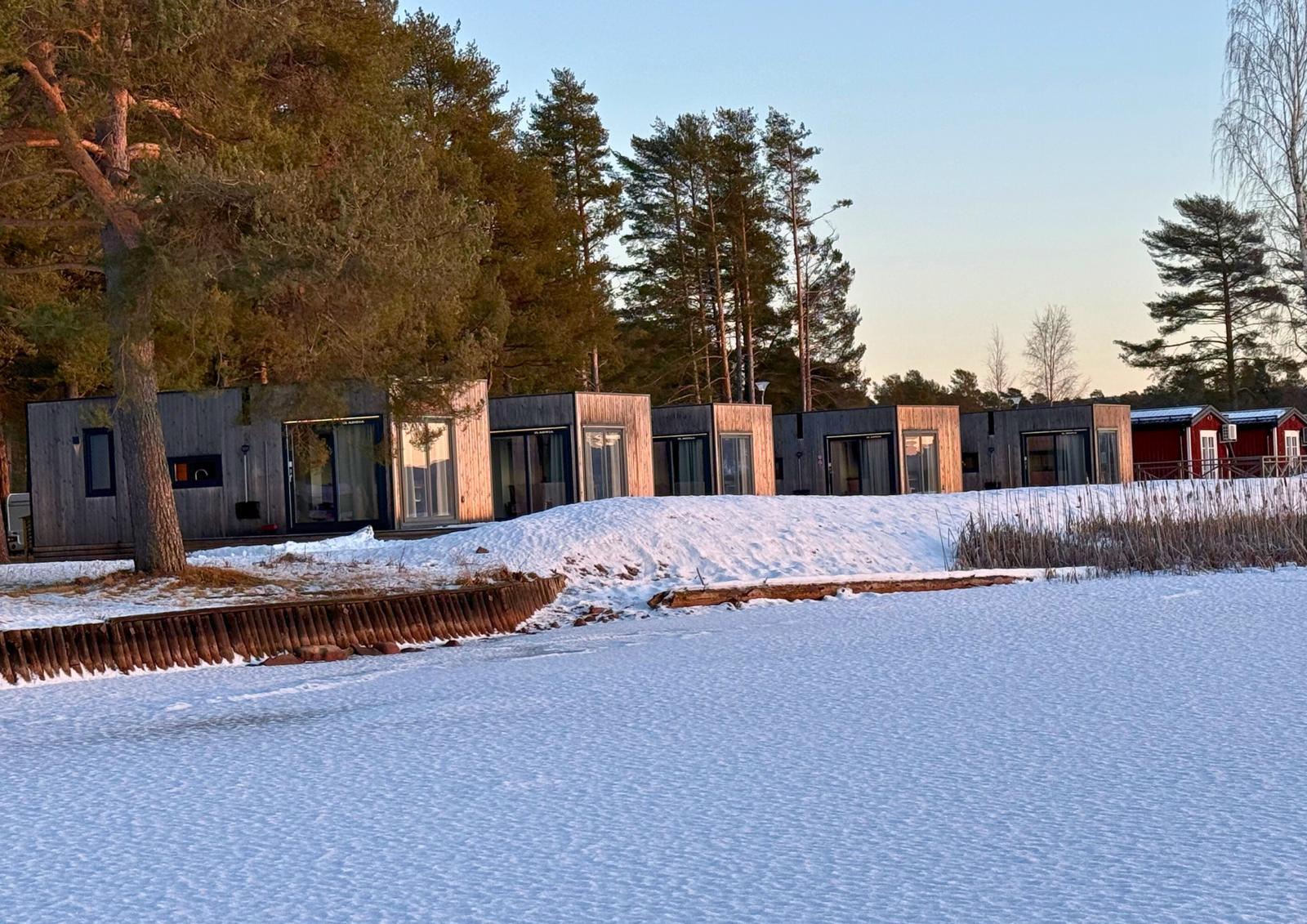 Houten huisjes in de sneeuw bij het bevroren Orsameer in Dalarna